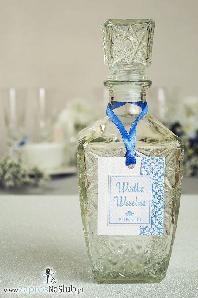 Zawieszki na alkohol z błękitno-białym florystycznym ornamentem po prawej, przyklejanym motywem tekstowym i błękitną wstążką